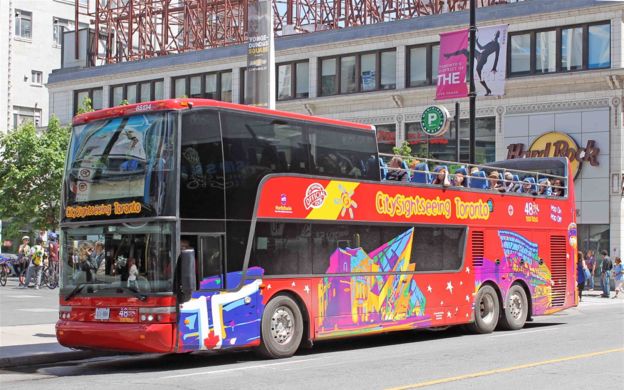 A vibrant red Hop-on Hop-off bus filled with ecited tourists, ready to explore the undiscovered wonders of the city Toronto.